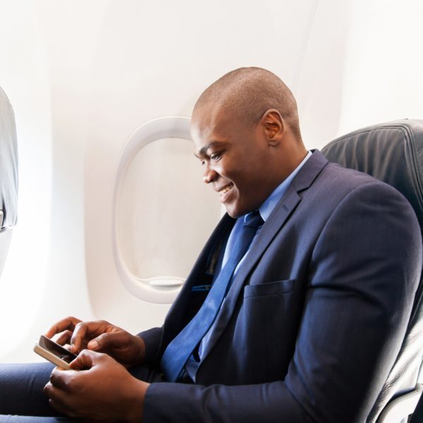 happy african airplane passenger using smart phone on plane