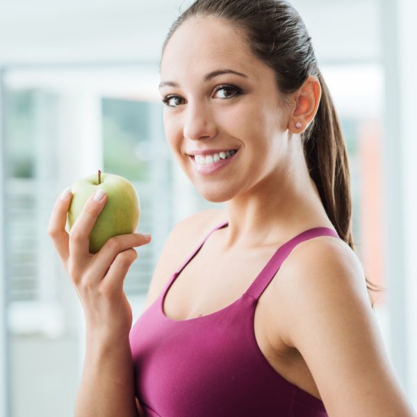 Young slim woman holding an apple and smiling at camera, healthy eating and weight loss concept